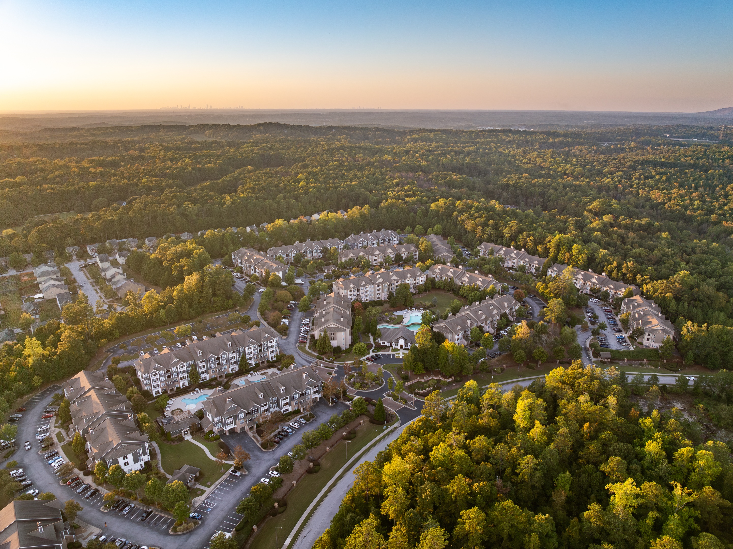 Sunlight hitting the Wesley Kensington apartment buildings nestled deep within a vast, dense green forest.